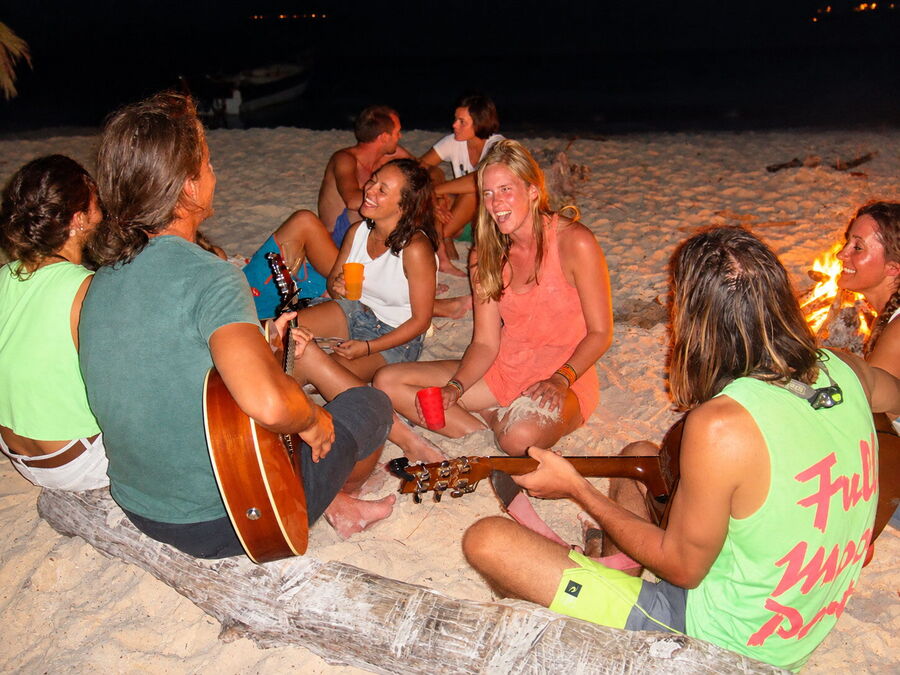 Viajeros con guitarras alrededor de una fogata en la playa de noche