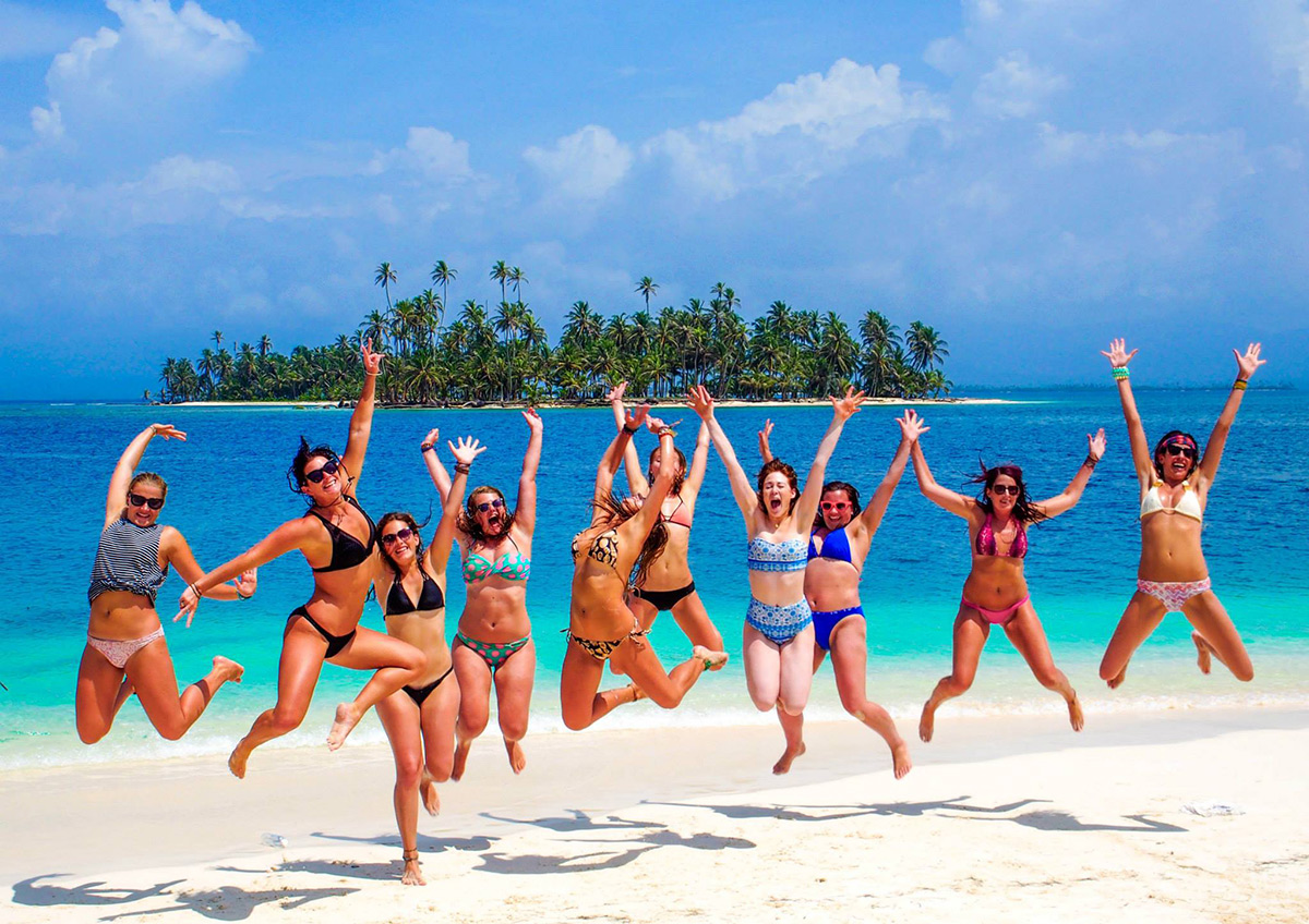 Group of travelers jumping on a beach with a palm-covered San Blas island behind them