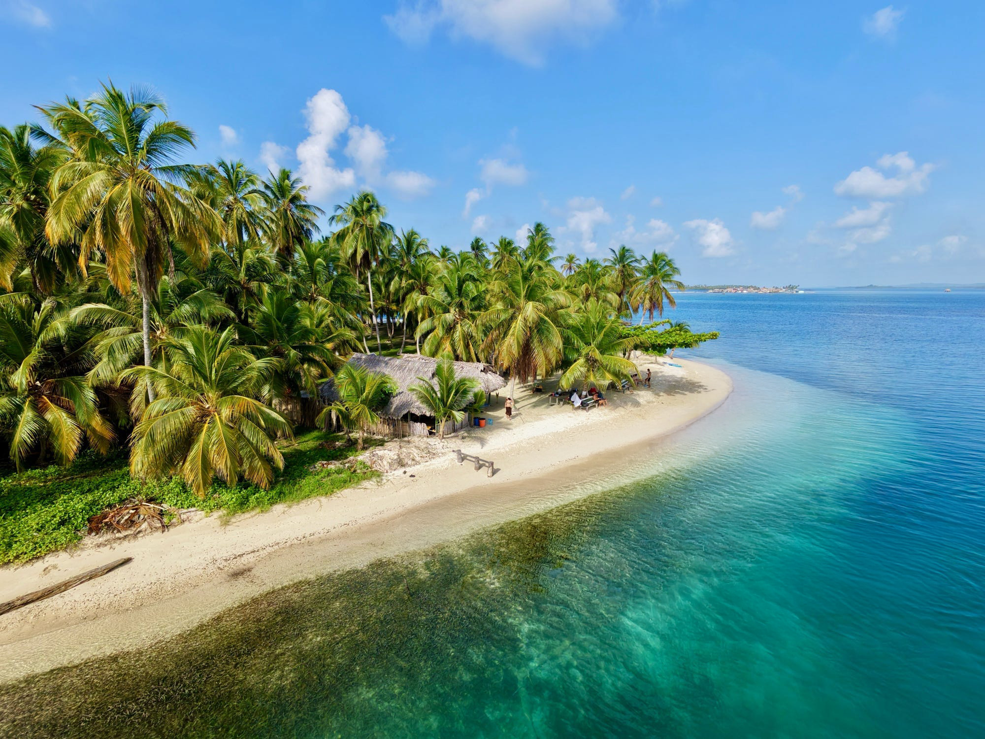 Aerial view of San Blas island with palm trees, white sand beach and San Blas Adventures boats in turquoise water