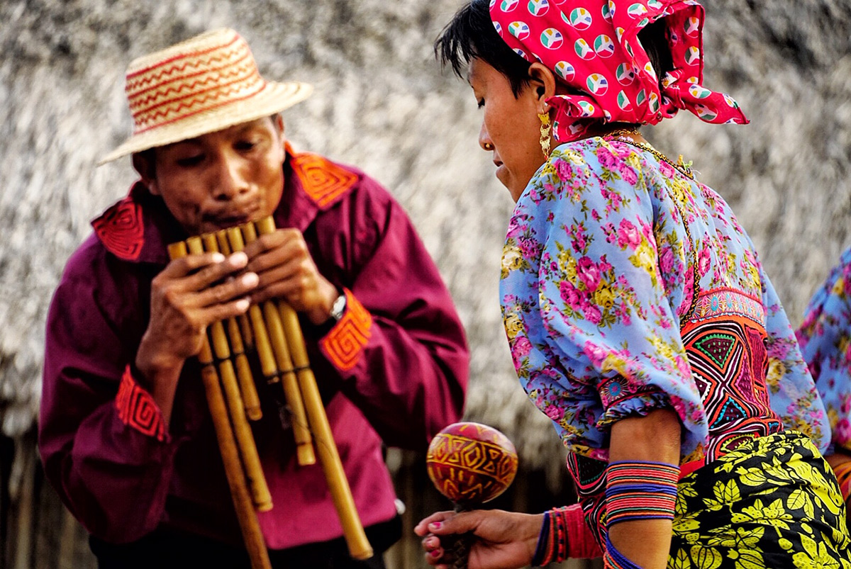 Guna man playing panpipes beside a Guna woman in traditional dress